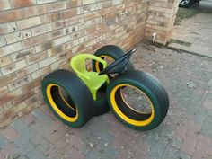 a green and yellow toy car sitting on top of a brick floor next to a wall