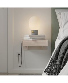 a nightstand with two books and a lamp on it next to a bed in a bedroom