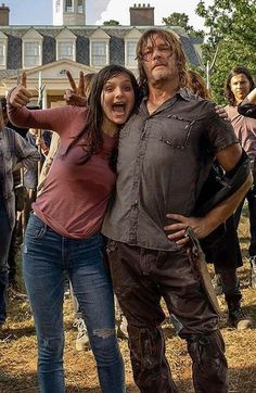 a man and woman posing for a photo in front of a house with zombies on it