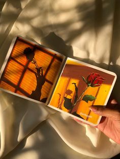 a person holding up an open book with flowers in the pages and shadows on it