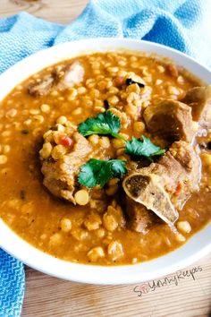 a white bowl filled with beans and meat on top of a wooden table next to a blue towel