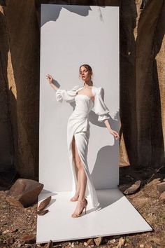 a woman standing in front of a white backdrop wearing a long dress and high heels