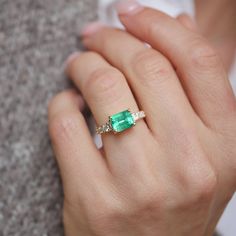 a woman's hand wearing a ring with an emerald and diamond accented band