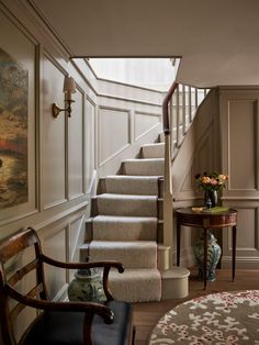 a staircase leading up to a living room and dining room area with blue chairs, rugs and paintings on the walls