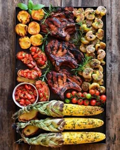 an overhead view of grilled meat, vegetables and potatoes on a platter with tomatoes