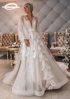 a woman standing in front of a couch wearing a white wedding dress with sheer sleeves