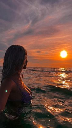 a woman sitting in the ocean at sunset