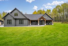 a large gray house sitting in the middle of a lush green field with lots of trees