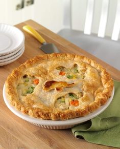 a chicken pot pie sitting on top of a wooden table next to plates and knives