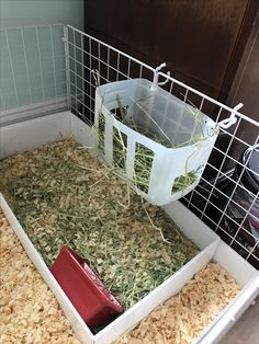 a caged area with hay in it and a red container on the floor next to it