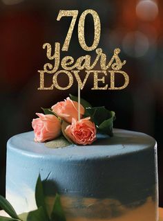 a blue cake with gold lettering and two pink roses on top is sitting on a table