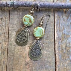 Boho brass and earthy green Czech glass dangle earrings.Small and lightweight, these brass earrings feature a small, swirled, earthy green and brown Czech glass bead and various shapes of brass dangles. The warm, light and neutral colors of these earrings make them a perfect everyday pair.Product overview:- Made with small Czech glass beads with various shapes of antiqued brass- Total hanging length of 2", the glass beads are approximately 0.5" in diameter- Very light weight and versatile- Hypoa Green Brass Earrings Nature-inspired, Earthy Metal Dangle Earrings, Rustic Brass Drop Earrings, Rustic Brass Dangle Earrings, Earthy Bronze Earrings With Ear Wire, Bronze Earthy Dangle Earrings, Earthy Green Dangle Earrings, Earthy Green Drop Earrings, Artisan Green Brass Earrings