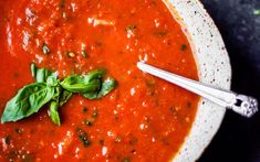 a bowl of tomato soup with basil on the side and a spoon next to it