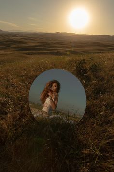 a woman standing in a field with her reflection in a mirror