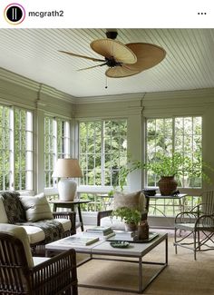 a living room filled with furniture and windows covered in wood shutters, surrounded by greenery