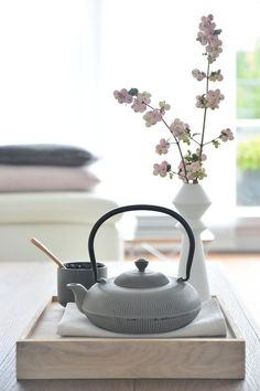 a tea kettle and cup on a tray with flowers in the vase next to it