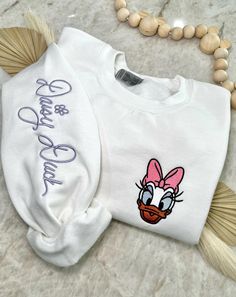 Cozy up in a bit of magic with our enchanting, Magical Autograph crewneck sweater. This sweater has a soft blended interior and features an embroidered face of the beloved Mrs. Duck on the left side of the chest and her autograph alongside the right sleeve. It could not get any cuter than this! ✦Sweater design features two embroidered locations. ✦Choose your preferred colored crew! ✦Interested in a different character? Head over to our "All Crewnecks" tab or type 'Magical Autograph Crewneck' in the search bar to see the other characters! ✦Want to pair this sweater with our mouse ears? Browse our ear selection to find your favorite match! White Letter Embroidery Sweater For Winter, White Crew Neck Sweater With Letter Embroidery, Cute White Embroidered Sweatshirt, Cute White Embroidered Sweater, White Embroidered Winter Tops, Winter White Embroidered Tops, Cute Winter Sweatshirt With Embroidered Text, Cute Crew Neck Embroidered Sweatshirt, White Embroidered Sweatshirt For Winter