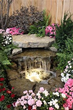 a garden with flowers, rocks and water features an artificial waterfall in the center surrounded by greenery