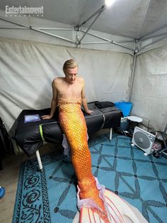 a man sitting on top of a bed next to a fake mermaid