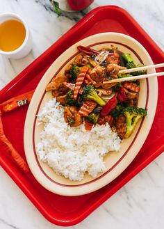 a plate with rice, broccoli and meat on it next to a cup of tea