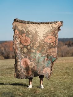 a woman standing in the grass holding up a blanket