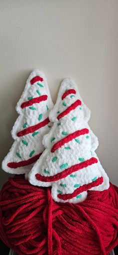 two crocheted christmas trees sitting on top of a ball of red and white yarn