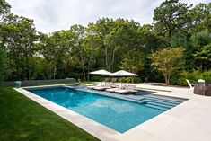 an empty swimming pool with lounge chairs and umbrellas in the middle, surrounded by trees