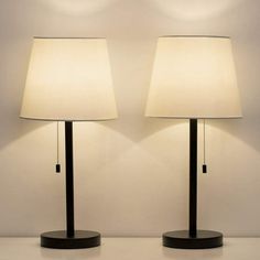 two lamps sitting next to each other on top of a white tablecloth covered floor