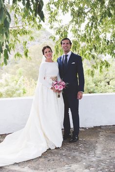 a bride and groom posing for a photo under a tree in front of a white wall