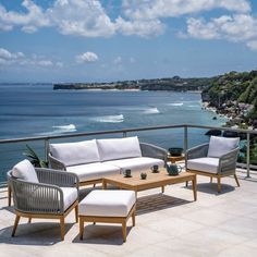 an outdoor seating area overlooking the ocean with white cushions and wicker furniture on it