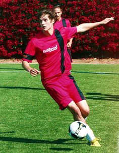 two young men are playing soccer on the green grass with red flowers in the background