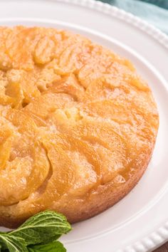 a pineapple upside down cake on a white plate next to some green leafy leaves