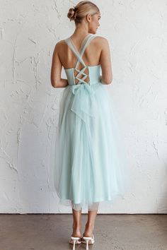 a woman in a blue dress standing against a white wall with her back to the camera