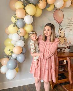 a woman holding a baby in front of balloons