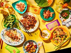 a yellow table topped with lots of plates and bowls filled with different types of food