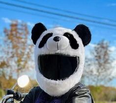 a stuffed panda bear sitting on the back of a motorcycle wearing a leather jacket and helmet