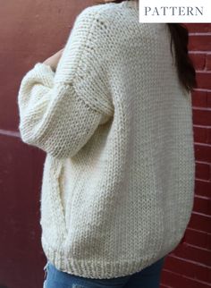 a woman wearing a white sweater and jeans is standing in front of a brick wall