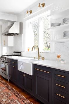 a kitchen with black cabinets, white counter tops and gold pulls on the sink area