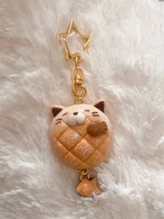 a cat keychain is laying on a white fur surface with a gold chain