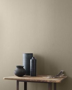 two vases are sitting on a wooden table in front of a green painted wall