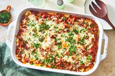 a casserole dish with meat, cheese and vegetables on it next to two wooden spoons