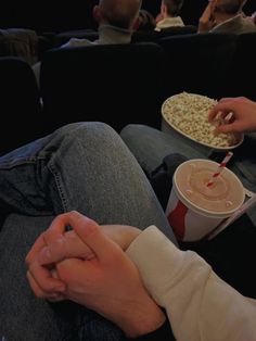 two people are sitting on the couch eating popcorn and drinking soda while watching movies together