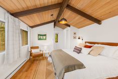 a bedroom with wood ceiling and white bedding in the middle of wooden flooring