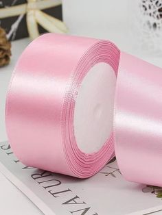 two rolls of pink satin ribbon sitting on top of a table next to a rose