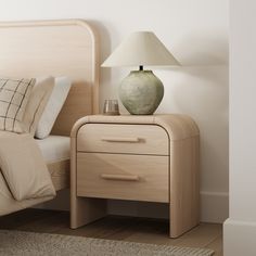 a nightstand with a lamp on top of it next to a bed