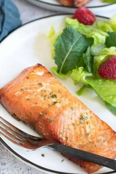 two plates with salmon, salad and raspberries on them are ready to be eaten