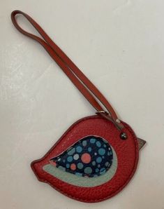 a red purse with a blue and white bird on it's side hanging from a brown leather strap