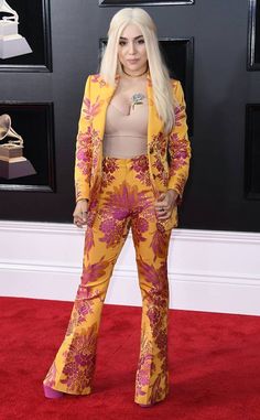 lady in yellow and pink outfit standing on red carpet with her hands behind her back