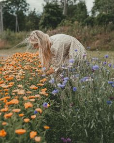 a woman is picking up flowers in the middle of a flower bed with long blonde hair