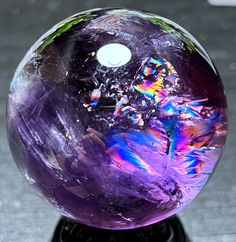 a purple marble ball sitting on top of a black stand with lots of colorful paint